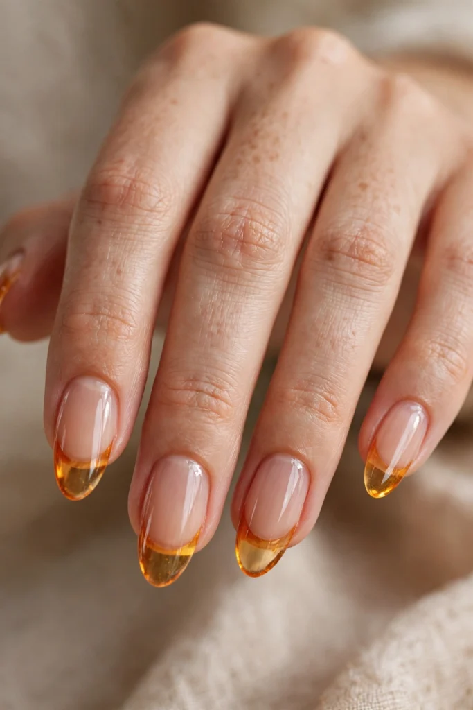 Close-up of almond nails with translucent amber-orange jelly French tips and a glassy gel look
