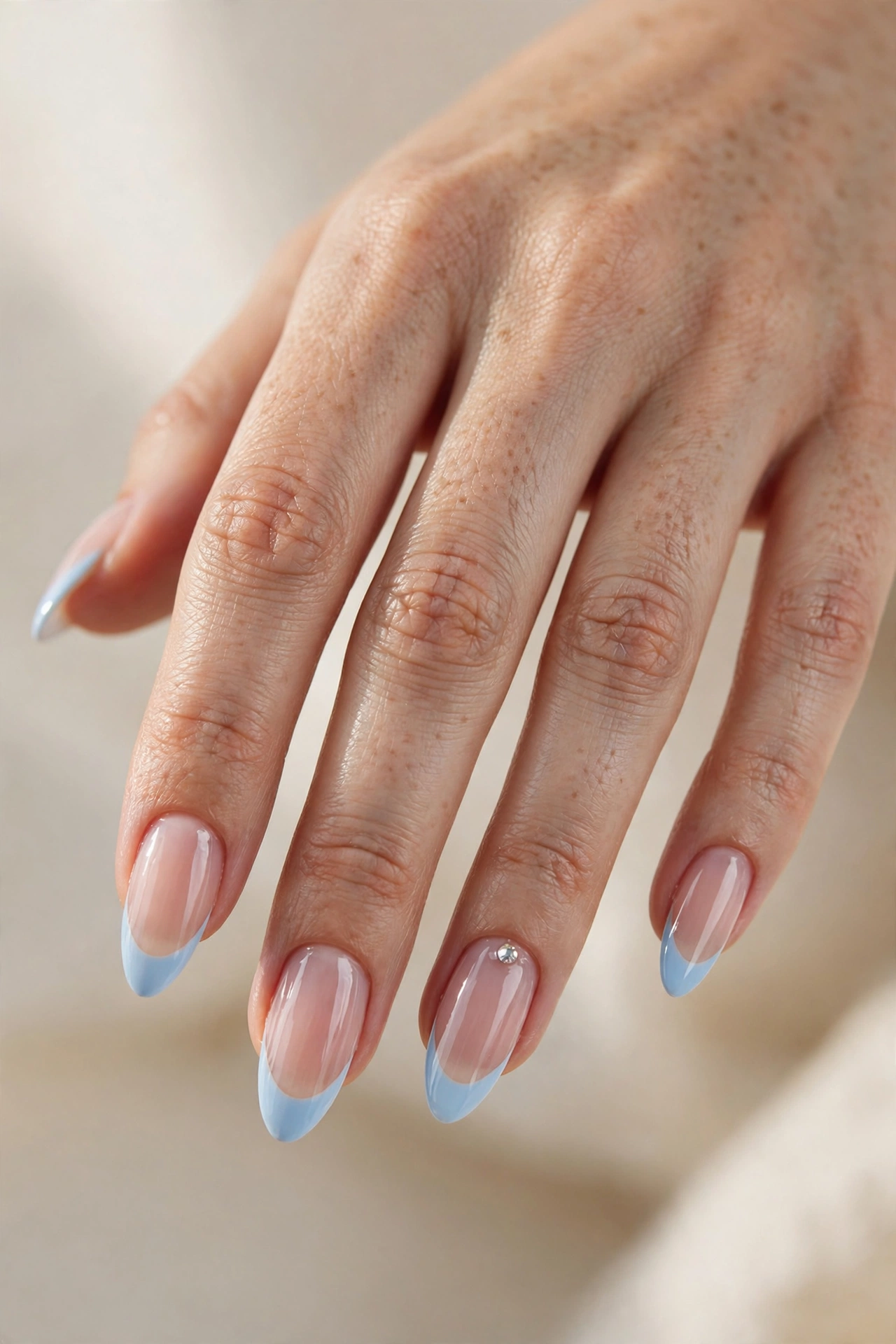 Long almond nails with glossy baby blue French tips and a single crystal rhinestone accent.
