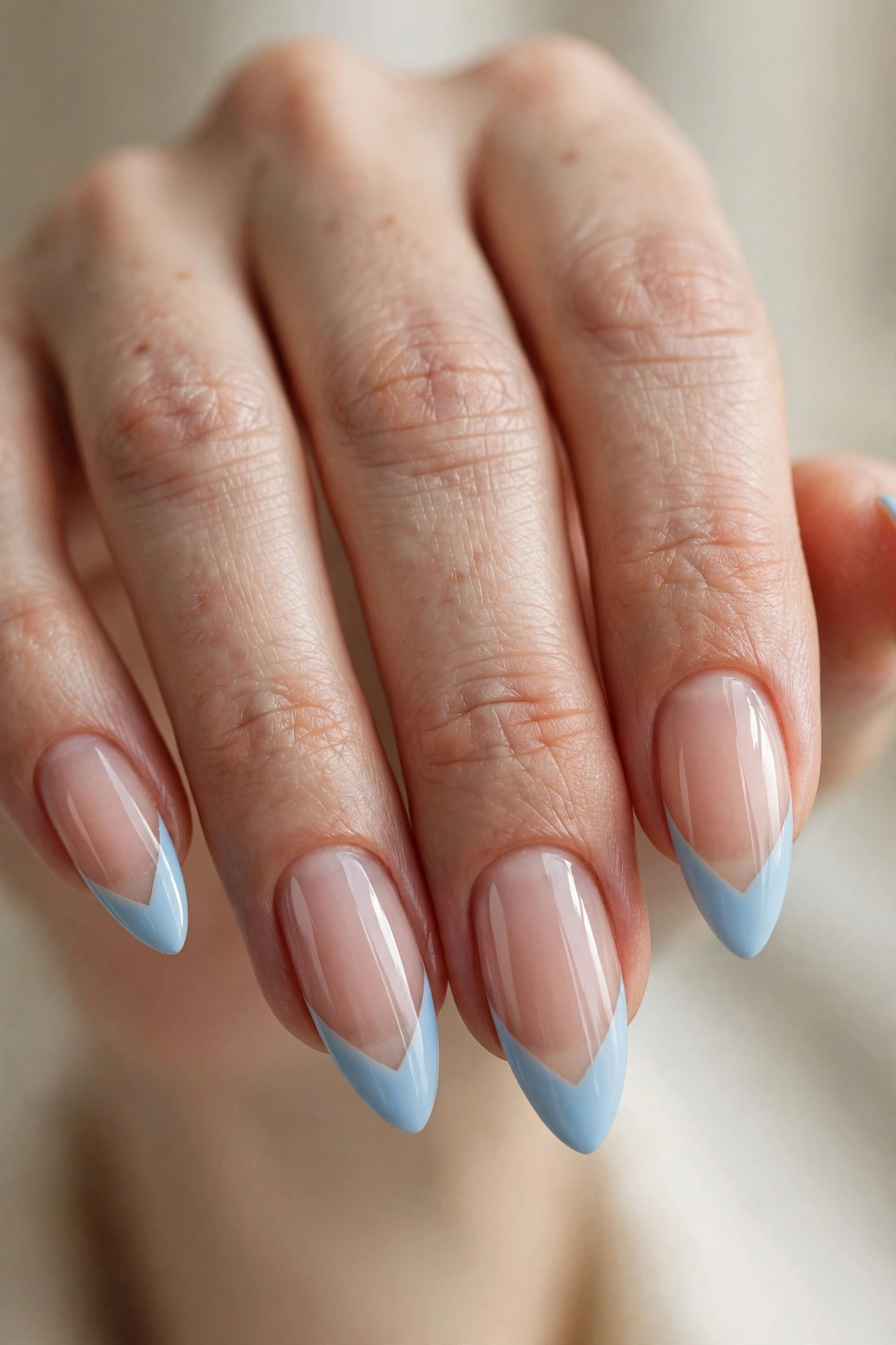 Long almond nails with baby blue V-shaped French tips over a sheer nude base.