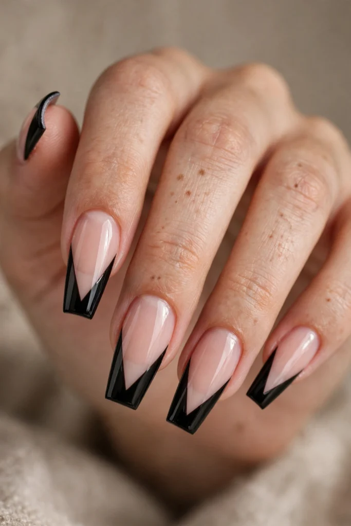 Close-up of long coffin-shaped nails with a glossy nude-pink base and sharp geometric black V-cut French tips.