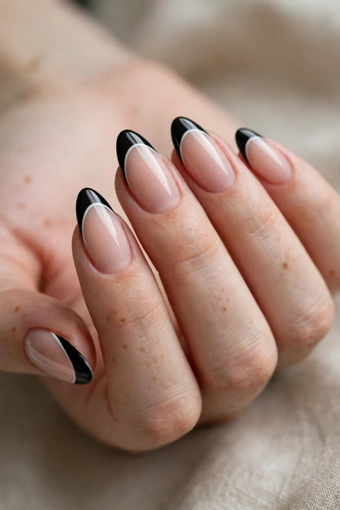Close-up of almond-shaped nails with nude bases, black French tips separated by a thin crisp white outline for a bold graphic look.
