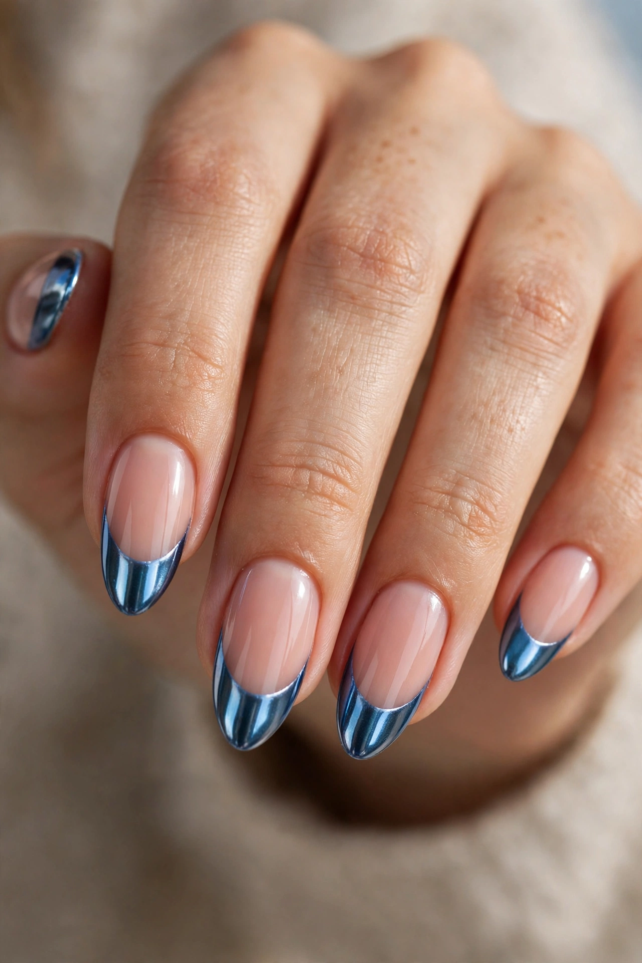 Close-up of almond nails with metallic blue chrome French tips with a reflective mirror finish.