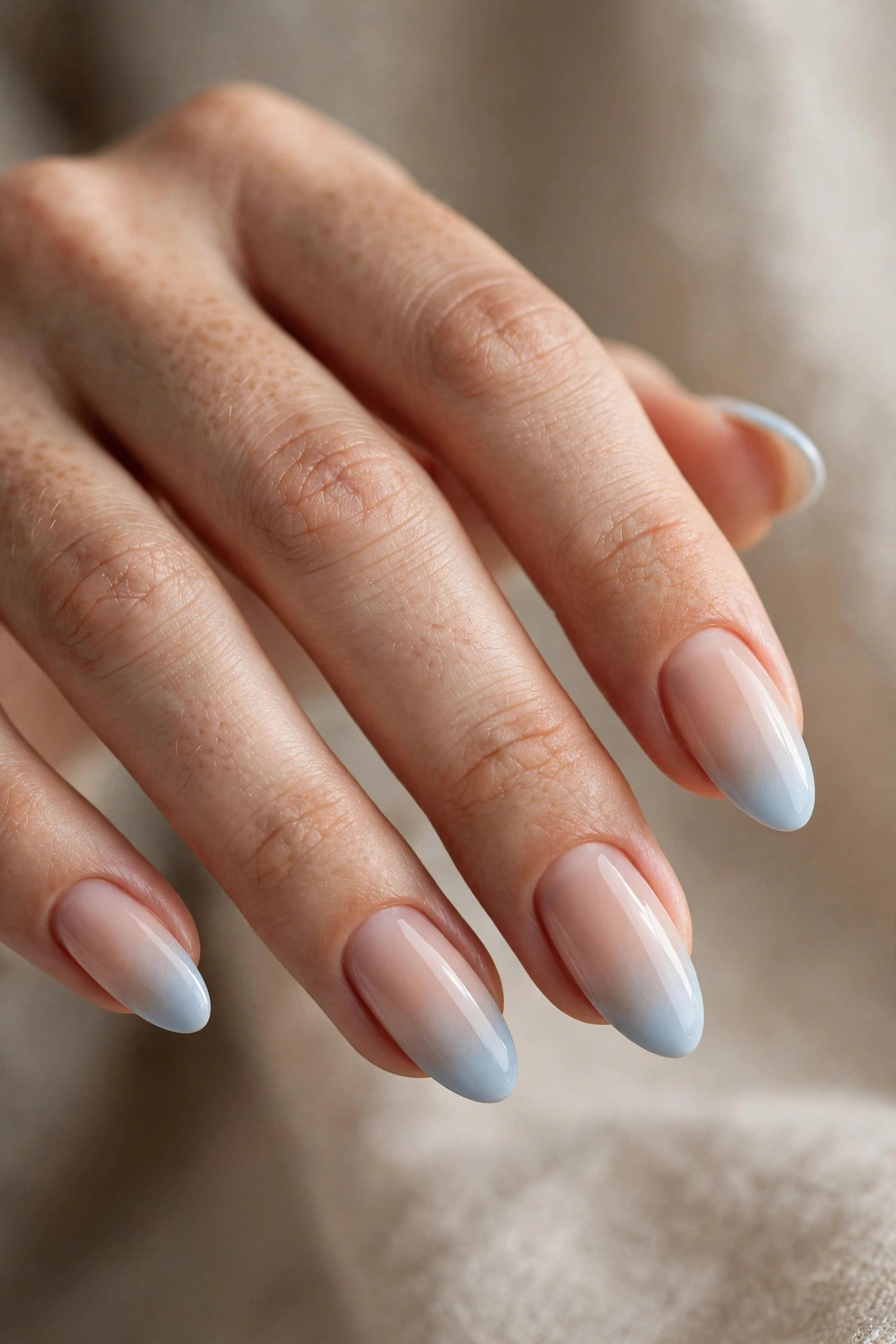 Close-up of almond nails with light blue ombre French tips fading from a nude base.