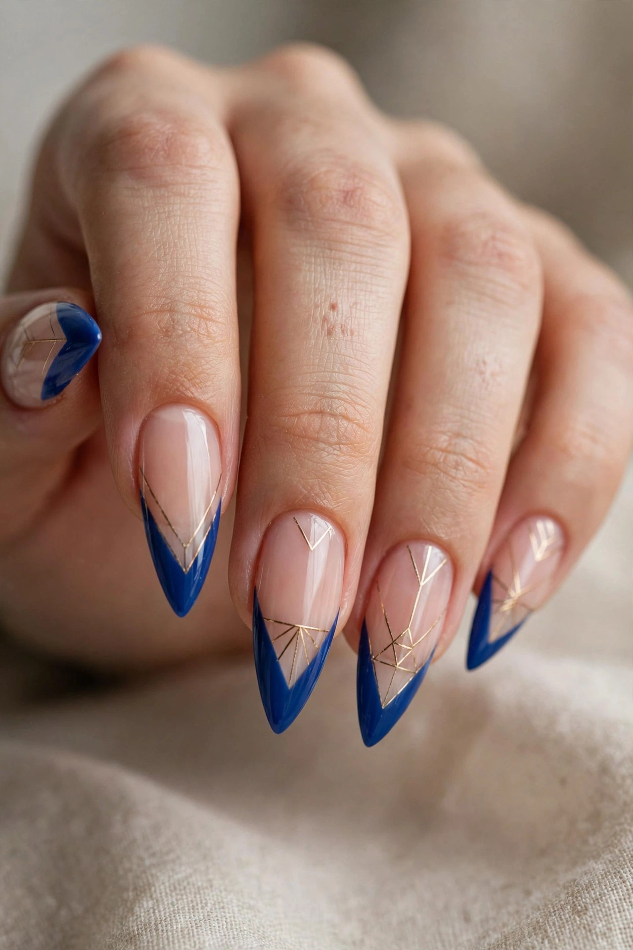 Close-up of stiletto nails with deep blue V-cut French tips accented with fine gold geometric lines.