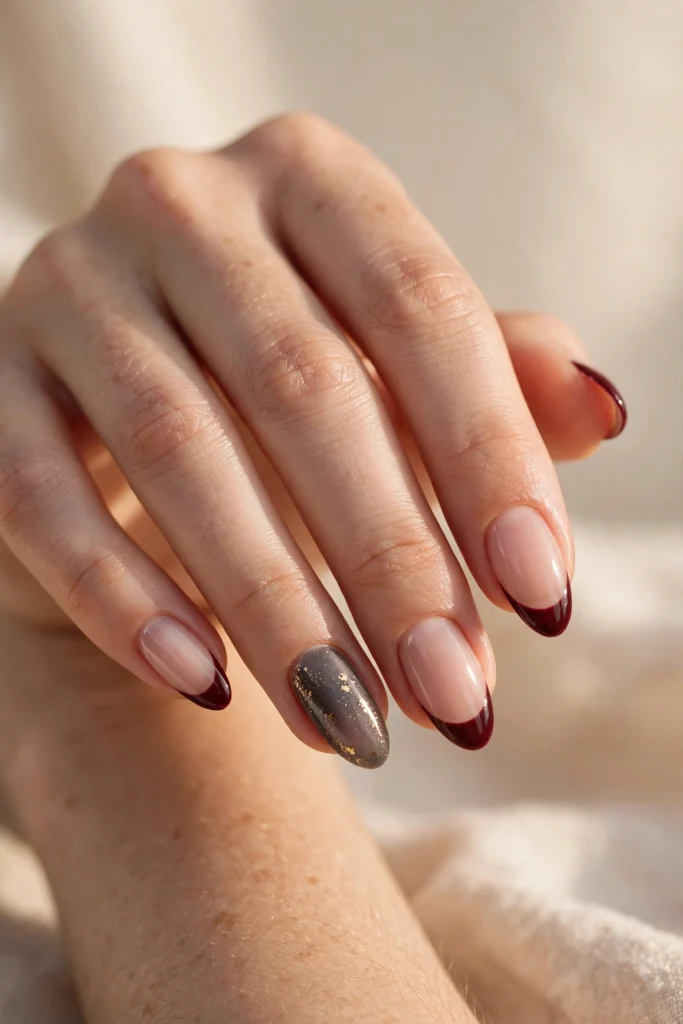 Almond nails with burgundy French tips and a smoky gray accent nail sprinkled with gold flecks.