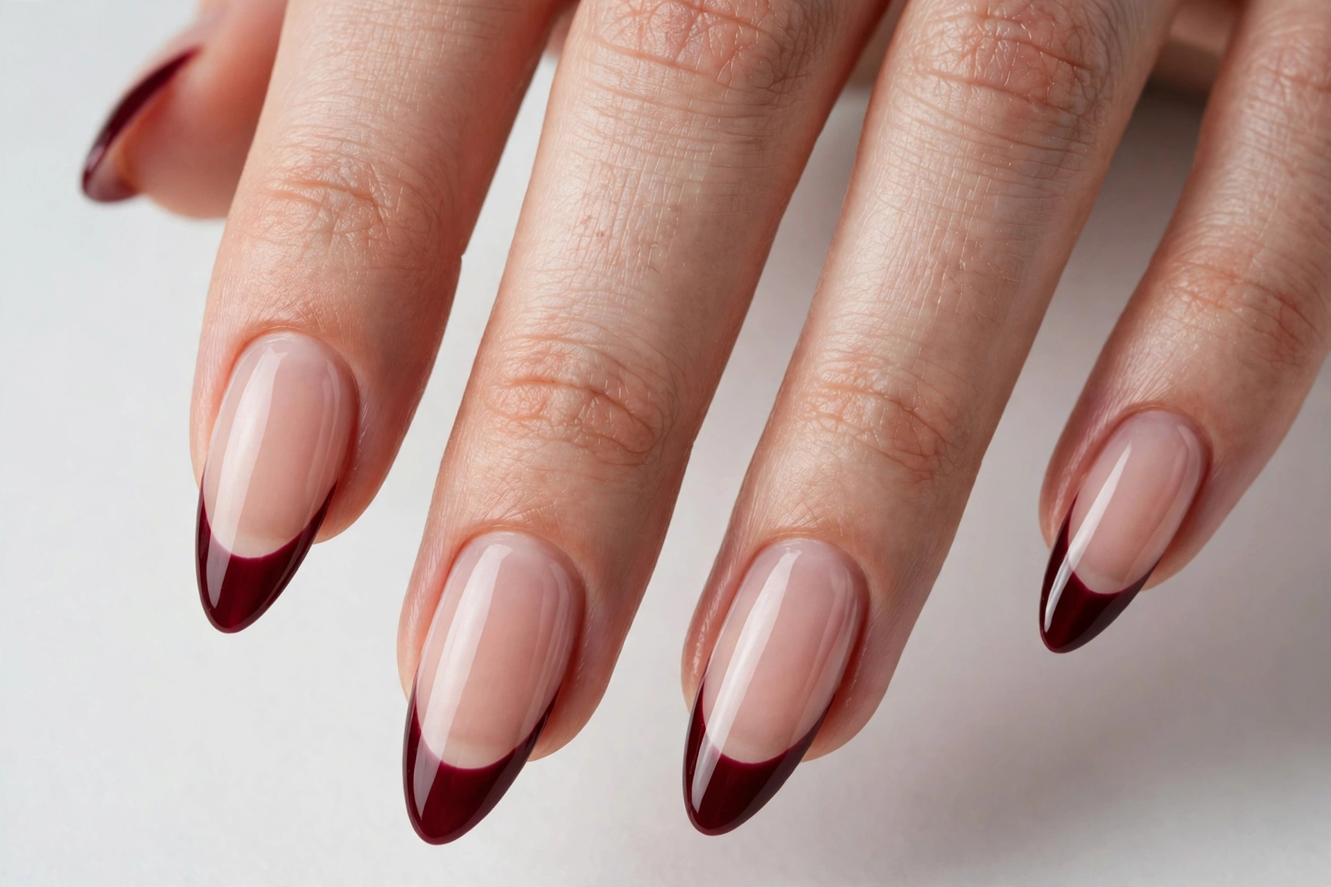 Christmas French tip nails with deep burgundy glossy tips on a sheer nude base, shown on long almond nails.