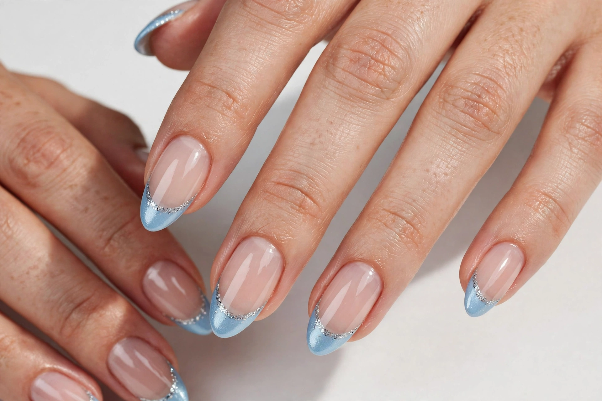 Christmas French tip nails with icy blue tips and silver glitter accents on a sheer base, shown on medium almond nails.