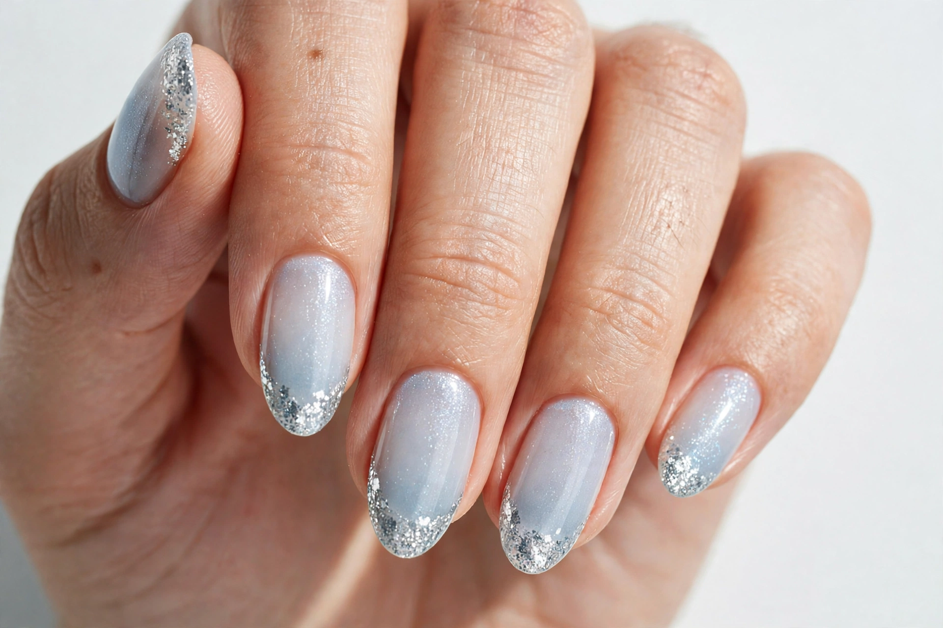 Christmas French tip nails with silver glitter tips on a sheer icy base, shown on medium almond nails.
