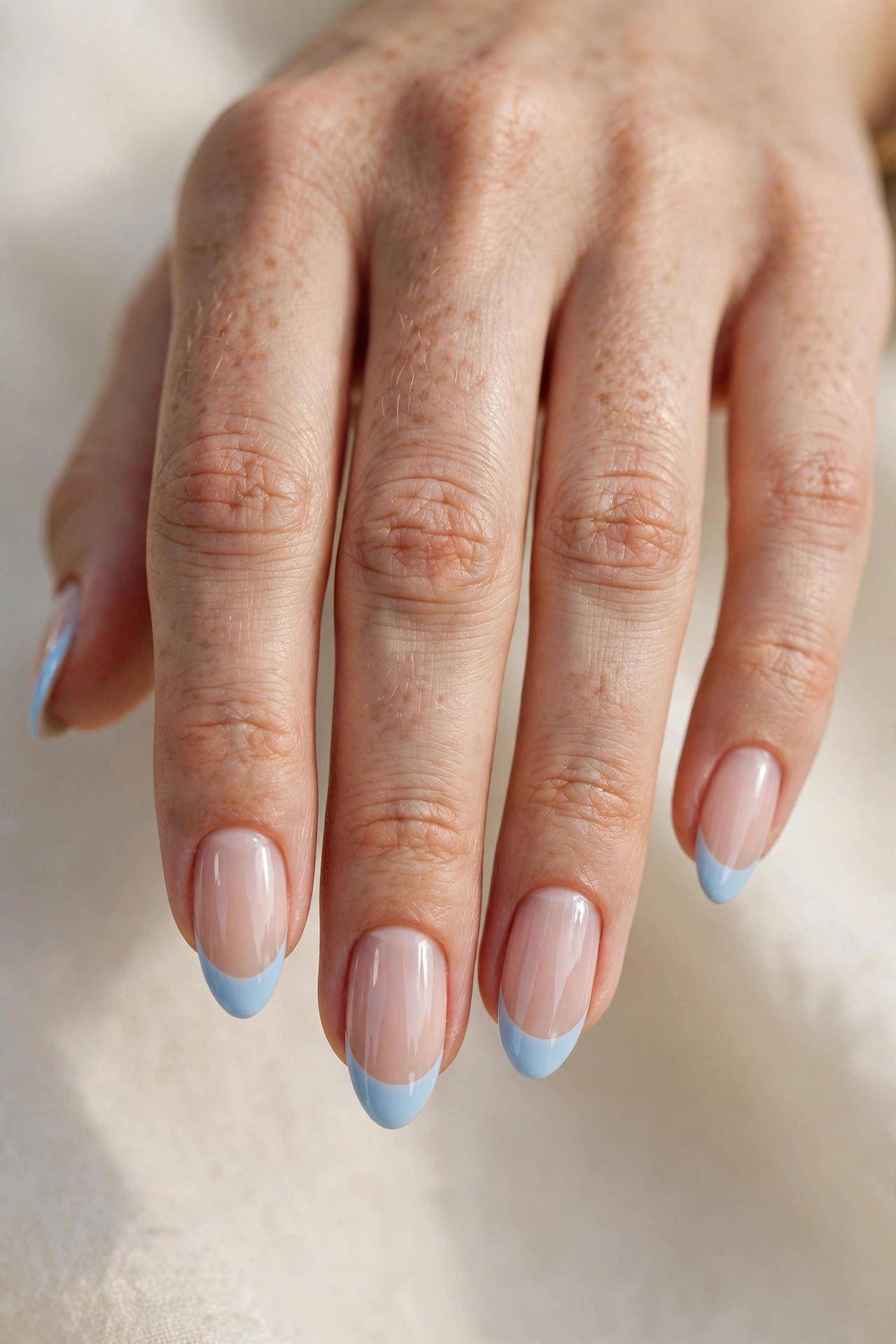 Close-up of almond nails with glossy baby blue French tips over a sheer nude base.