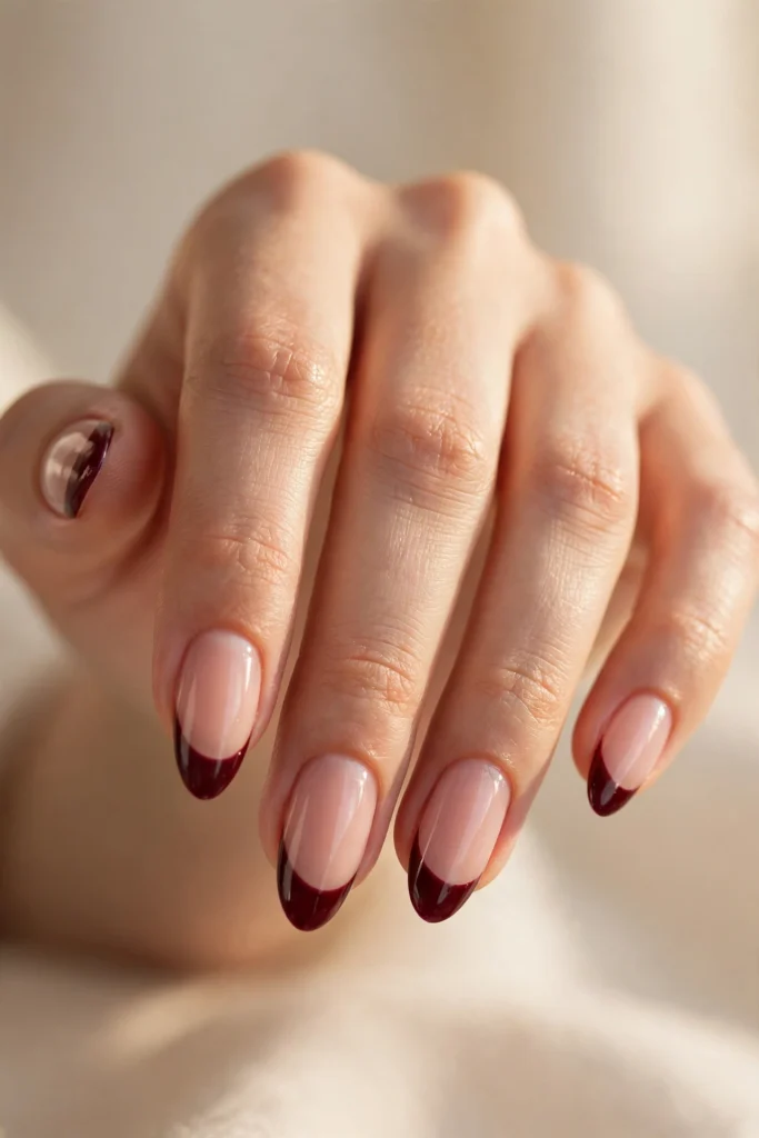 Close-up of almond nails with glossy deep-wine burgundy French tips over a sheer nude base.