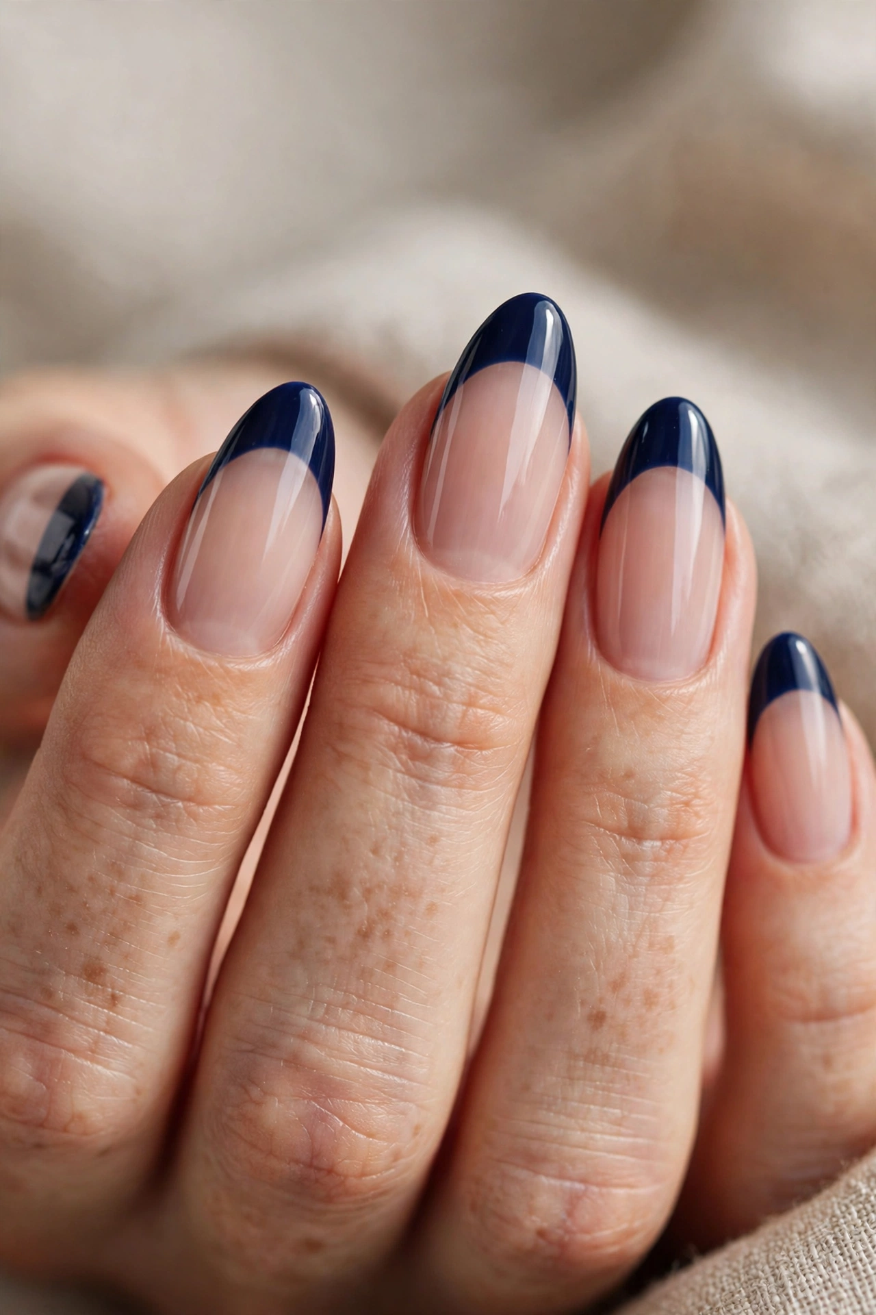 Close-up of almond nails with glossy deep navy French tips over a sheer nude base.