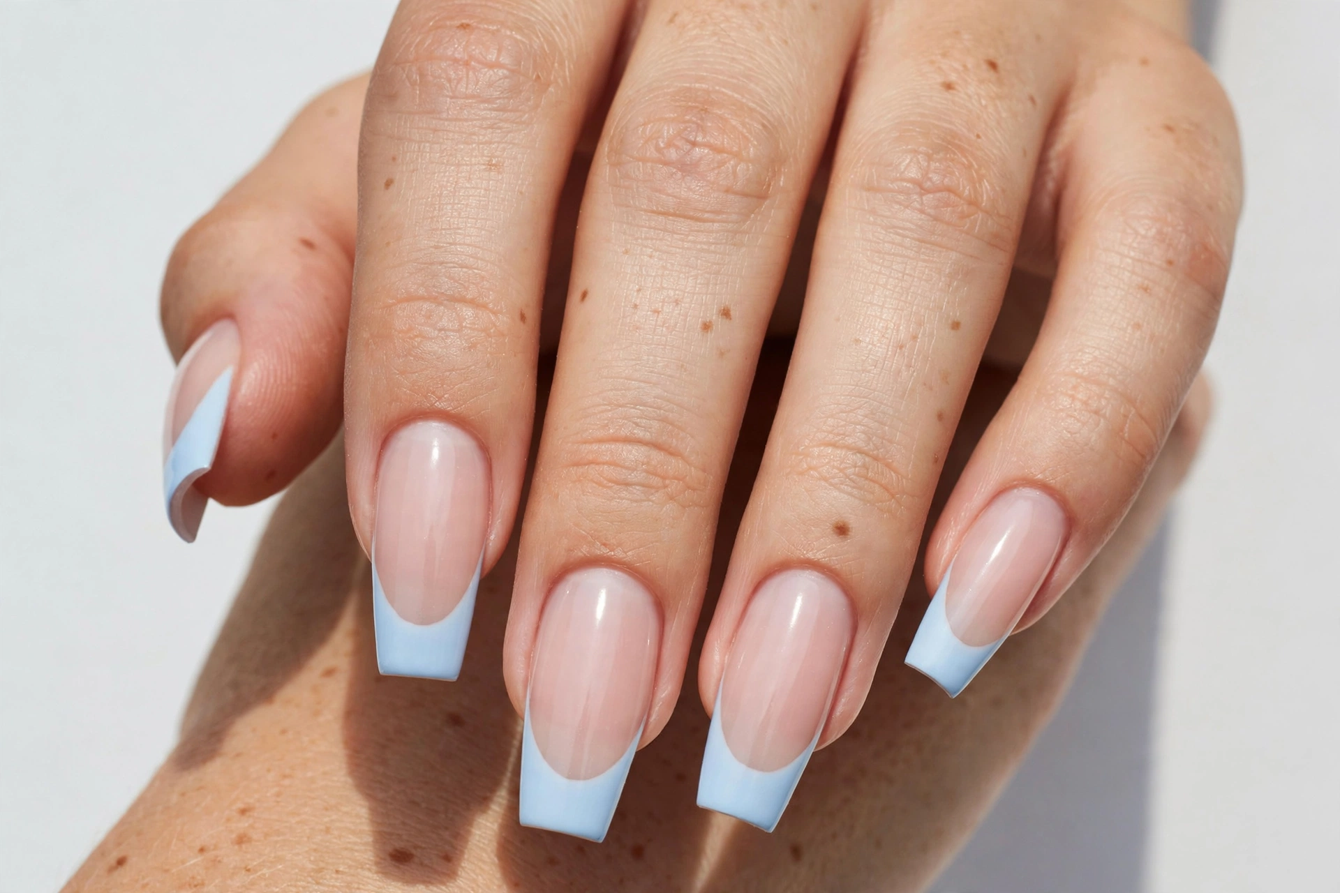 Coffin French tip nails with soft baby blue pastel tips on a sheer nude base, shown on medium coffin nails.
