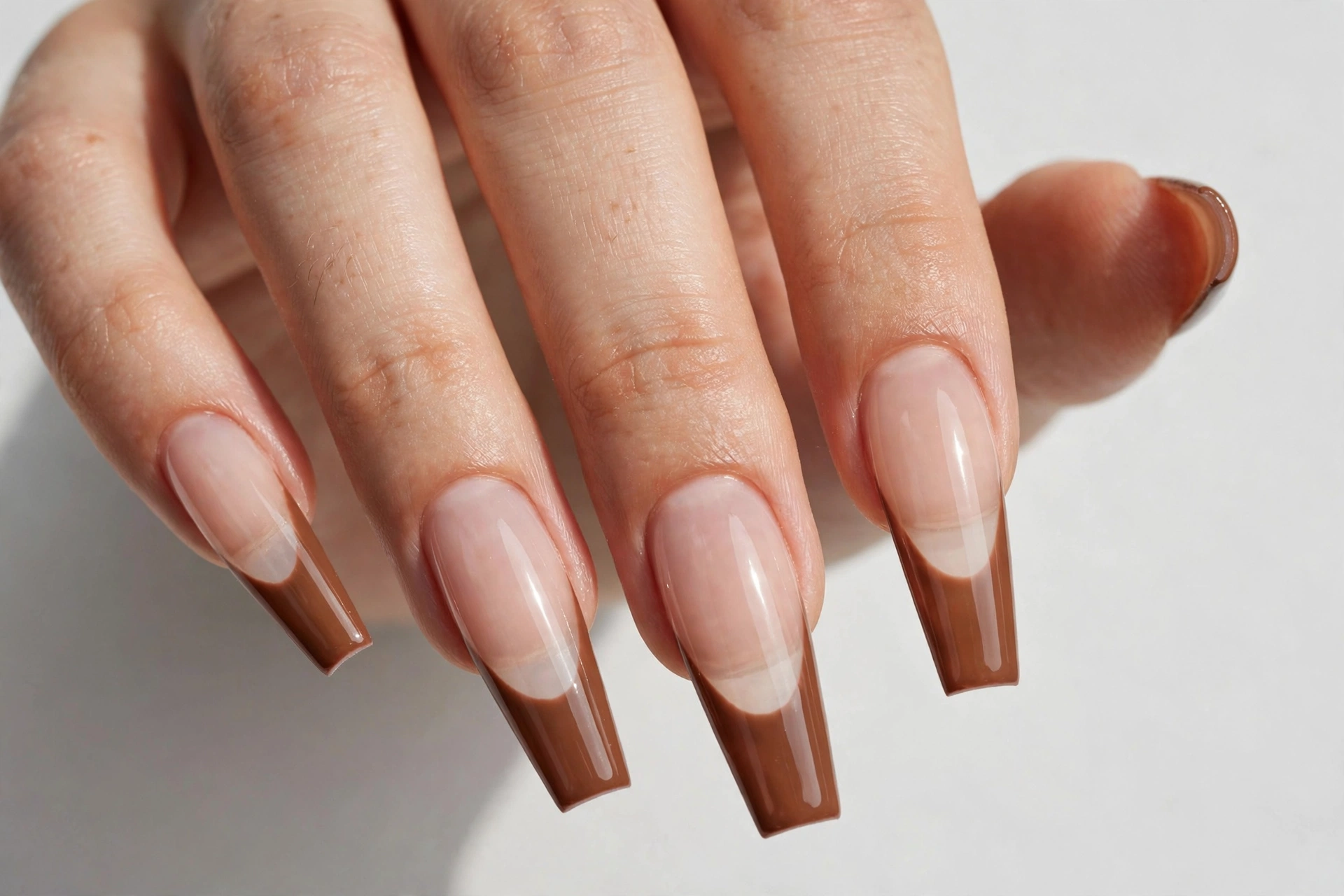 Brown coffin French tip nails with warm brown glossy tips on a sheer nude base, shown on long coffin nails.