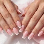 Coffin French tip nails with classic crisp white tips on a soft pink base, shown on a woman's hands against a white and soft pink background.