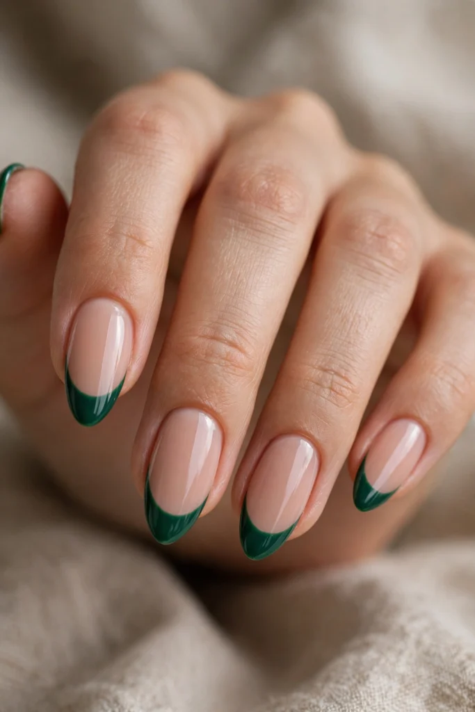 Close-up of almond-shaped nails with glossy emerald green French tips over a nude base.