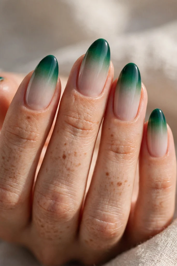 Almond nails with emerald green ombre French tips blending from a milky nude base into deep emerald at the edges.