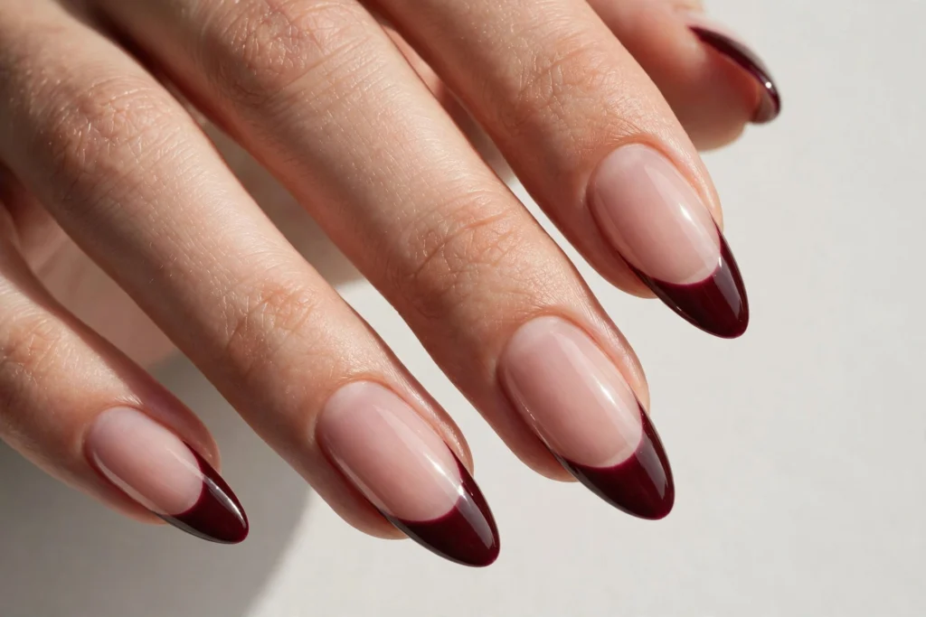 Fall French tip nails with deep burgundy glossy tips on a sheer nude base, shown on long almond nails.