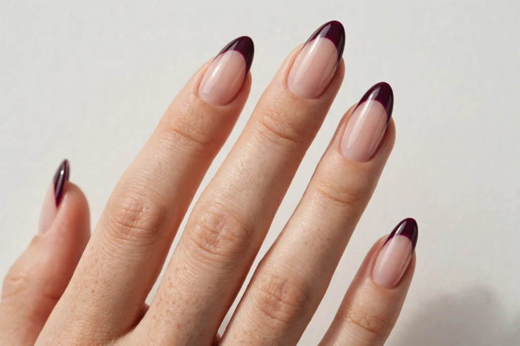 Fall French tip nails with deep plum glossy tips on a sheer nude base, shown on long almond nails.