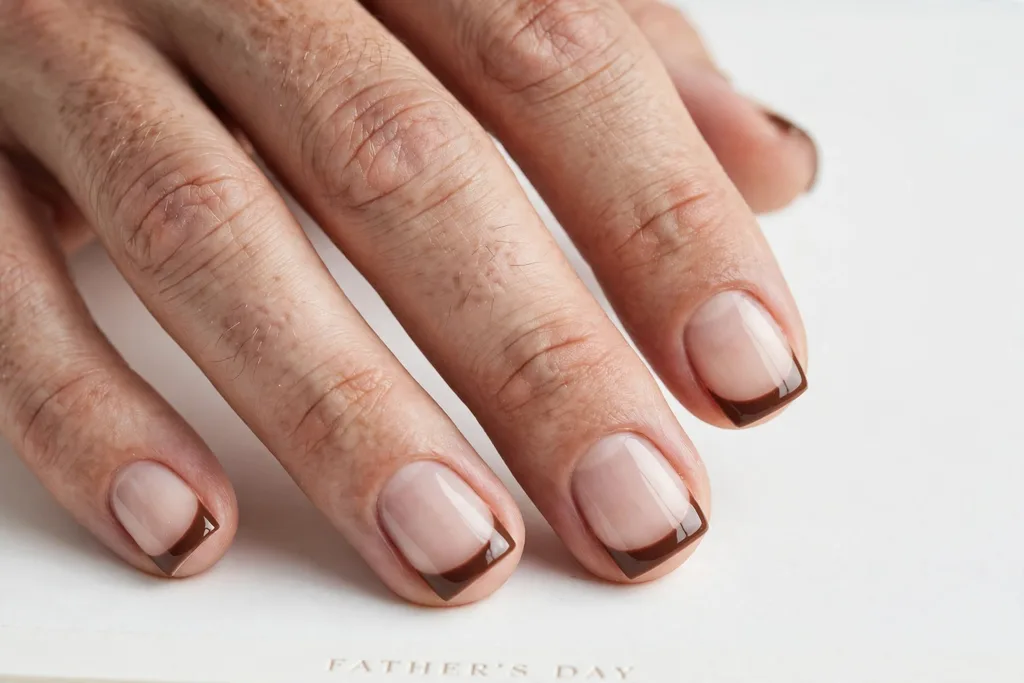 Father's Day French tip nails with chocolate brown glossy tips on a sheer natural base, shown on a man's hands with short square nails.