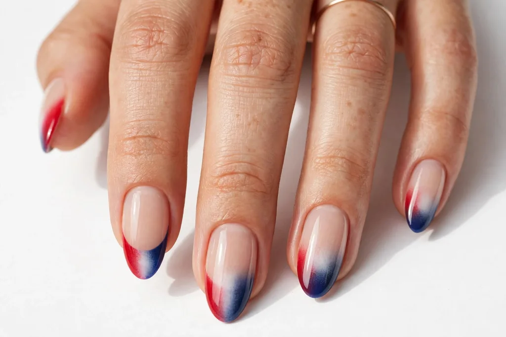 Red-to-Blue Ombre Fourth of July French Tip Nails Fourth of July French ombre nails with tips fading from red through white into navy blue over a sheer nude base, shown on medium almond nails.