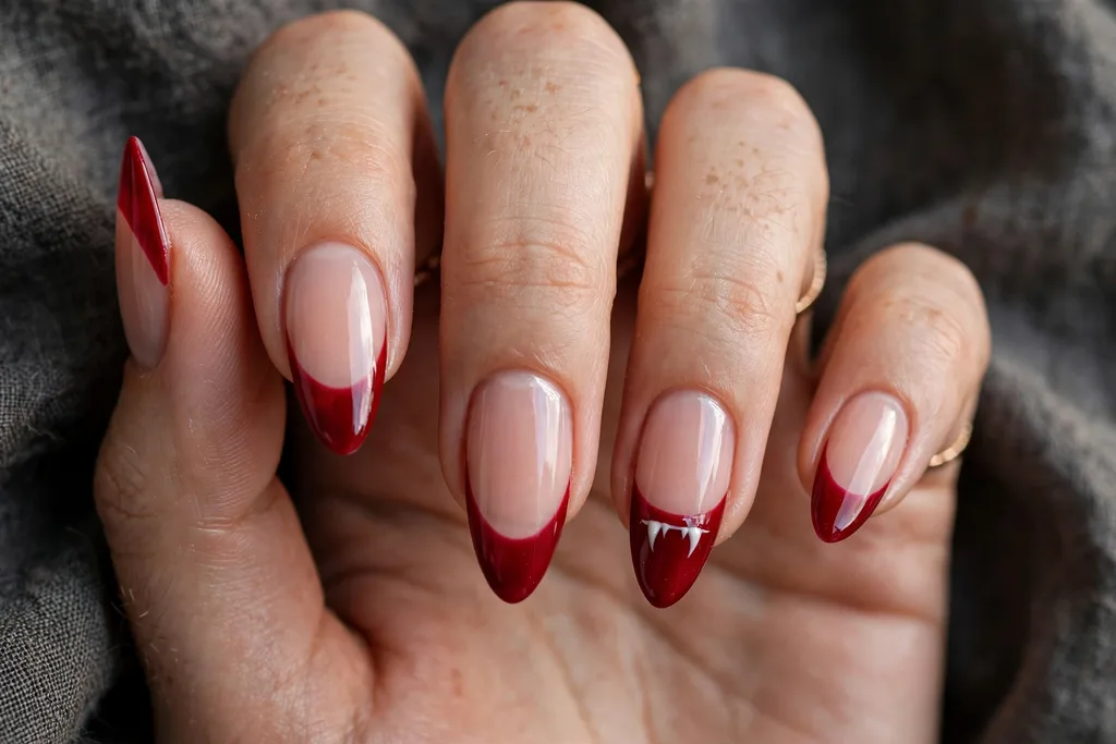 Halloween party French tip nails with blood red tips and two tiny white vampire fang points on each ring finger accent nail, shown on long almond nails.