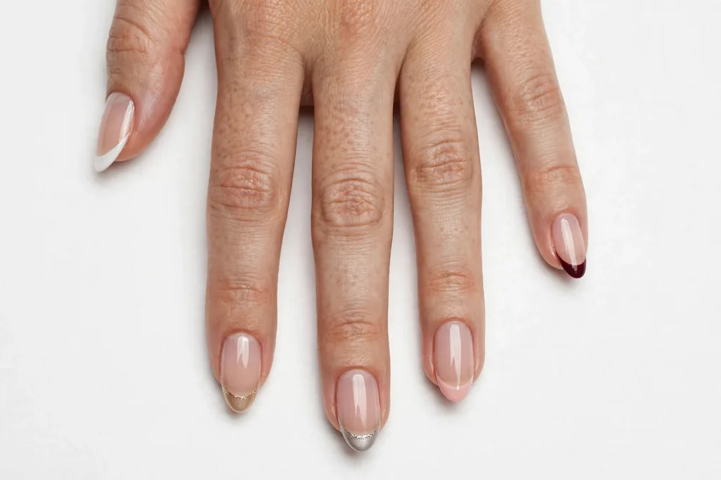 Five Shades of Winter Holiday Wedding French Tip Nails Holiday wedding French tip nails with a different winter tip color on each nail, including winter white, champagne, silver, blush, and burgundy, on a sheer nude base, shown on medium almond nails.