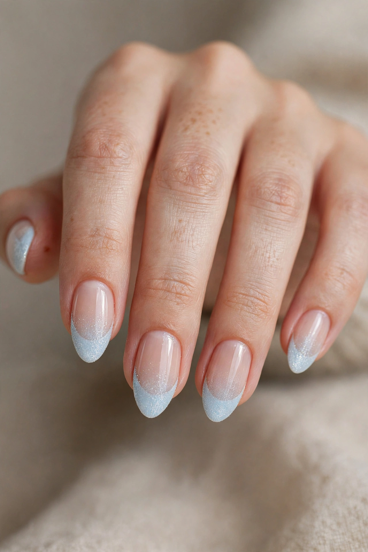 Close-up of almond nails with frosty icy pale-blue French tips with a shimmer finish.