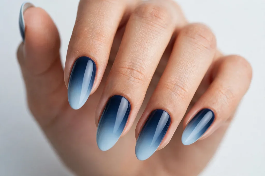 Labor Day French tip nails with tips fading from pale sky blue at the edge to deep navy near the base, shown on long almond nails.