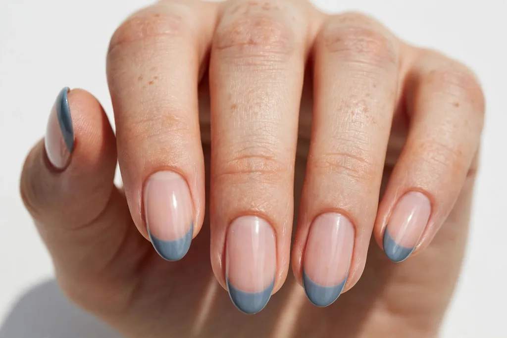 Memorial Day French tip nails with dusty blue-grey tips on a sheer nude base, shown on medium almond nails.