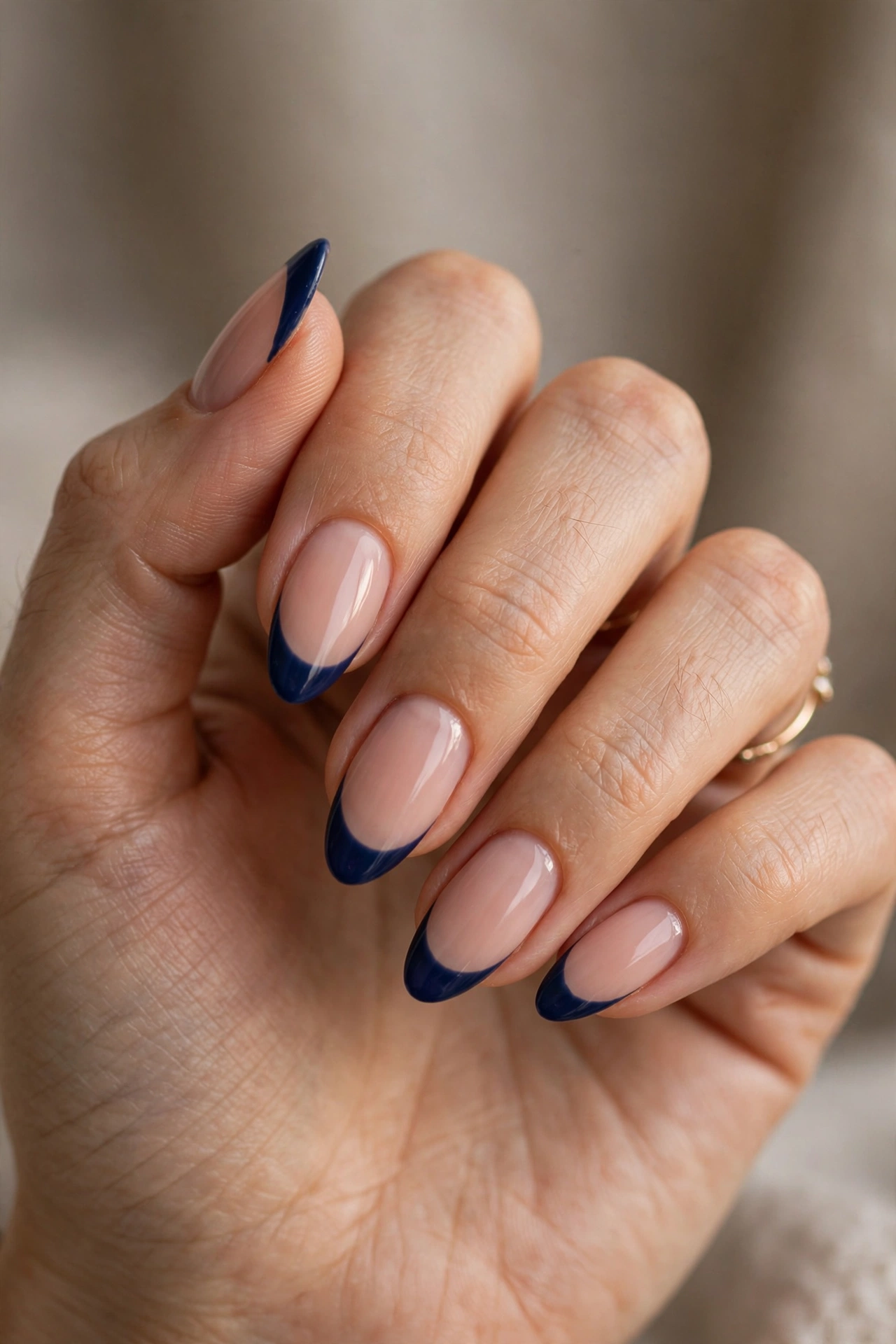 Close-up of almond nails with deep navy blue French tips over a nude base.