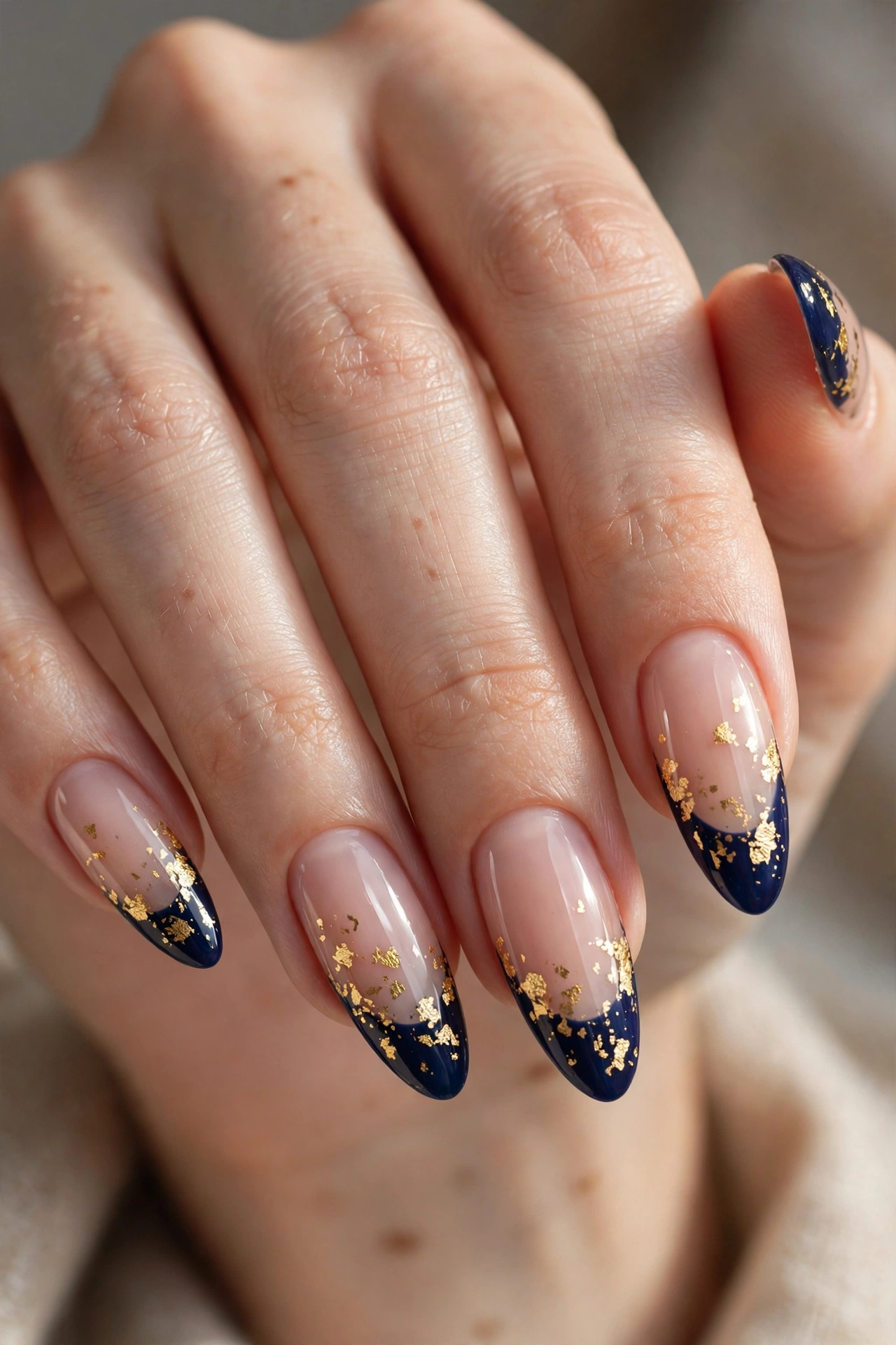 Long almond nails with deep navy French tips scattered with irregular gold foil flecks.