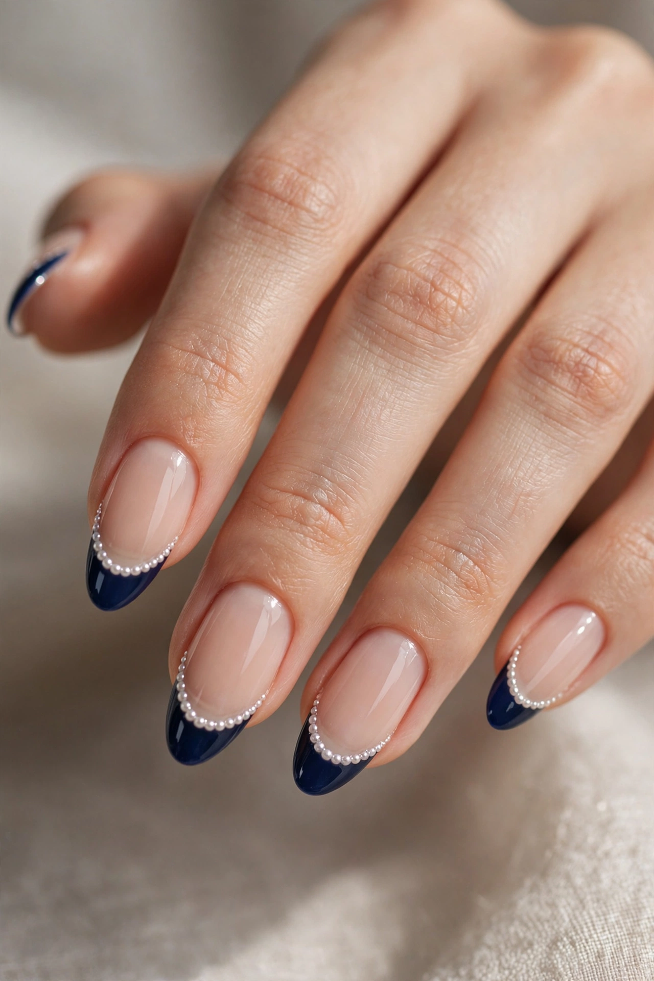 Almond nails with deep navy French tips decorated with tiny white pearls along the smile line.