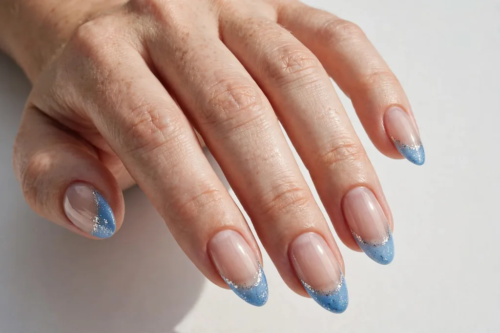 New Year's Eve French tip nails with icy blue tips and silver glitter accents on a sheer base, shown on medium almond nails.