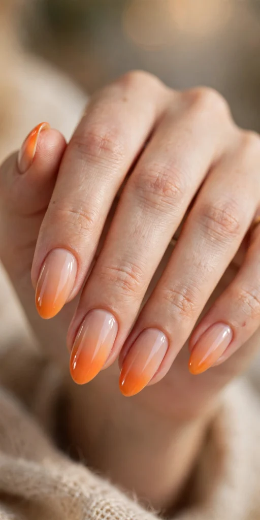 Close-up of almond nails with an orange ombre French fade blending from nude into tangerine orange tips