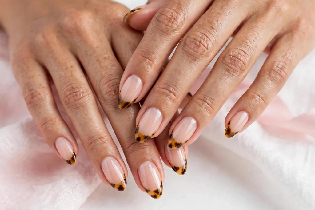 Thanksgiving dinner French tip nails with tortoiseshell tips in mottled amber, caramel, and dark brown on a sheer nude base, shown on medium almond nails.