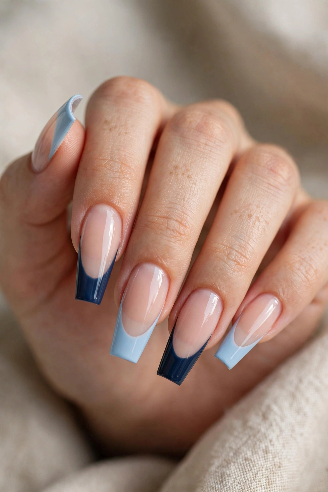 Close-up of long coffin nails with two-tone French tips alternating light blue and dark navy.