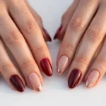Valentine date night French tip nails with deep red, burgundy, and rose gold tips and glossy romantic finishes on a sheer nude base, shown on a woman's hands against a white background in soft evening light.