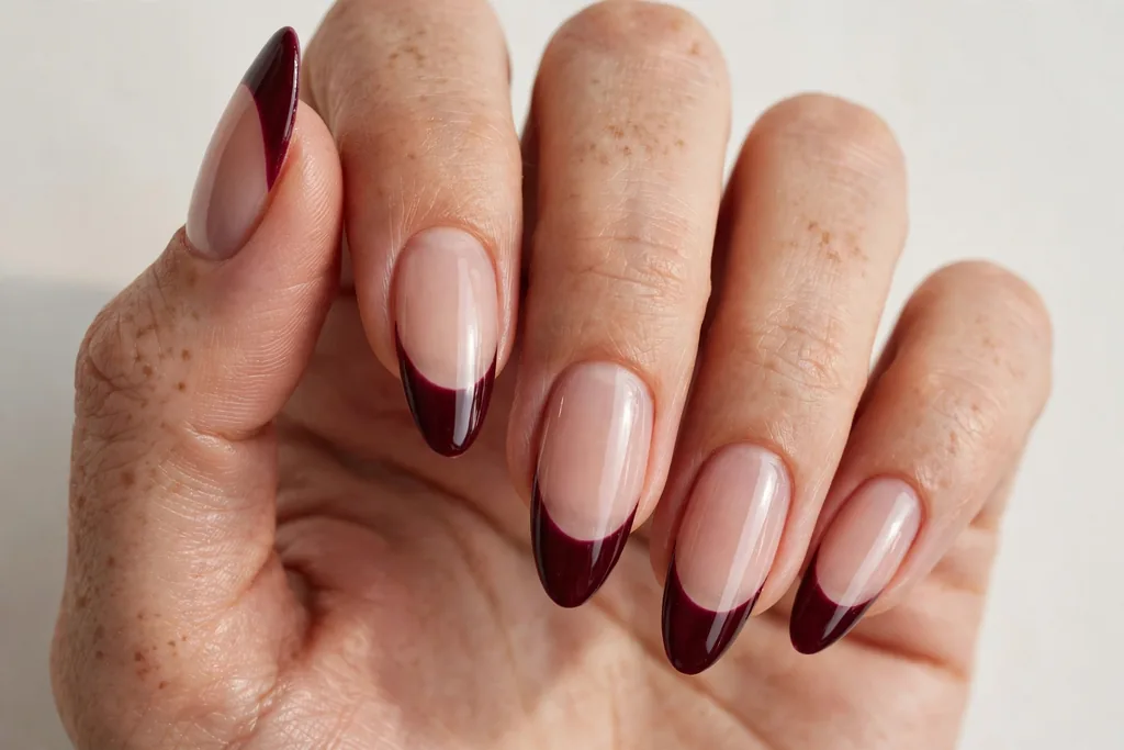 Valentine's Day French tip nails with deep wine burgundy glossy tips on a sheer nude base, shown on long almond nails.