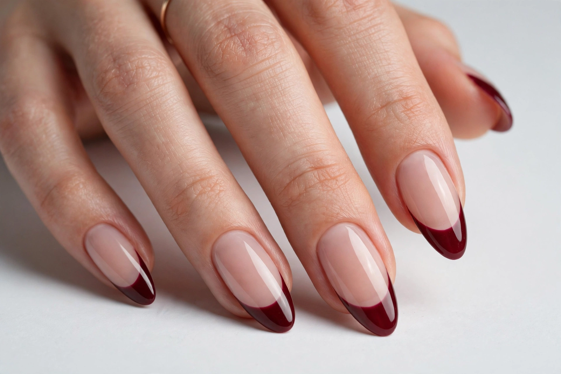 Winter French tip nails with deep burgundy glossy tips on a sheer nude base, shown on long almond nails.
