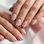 Winter French tip nails with icy white and silver chrome tips on a nude base, shown on a woman's hands against a white and soft pink background.