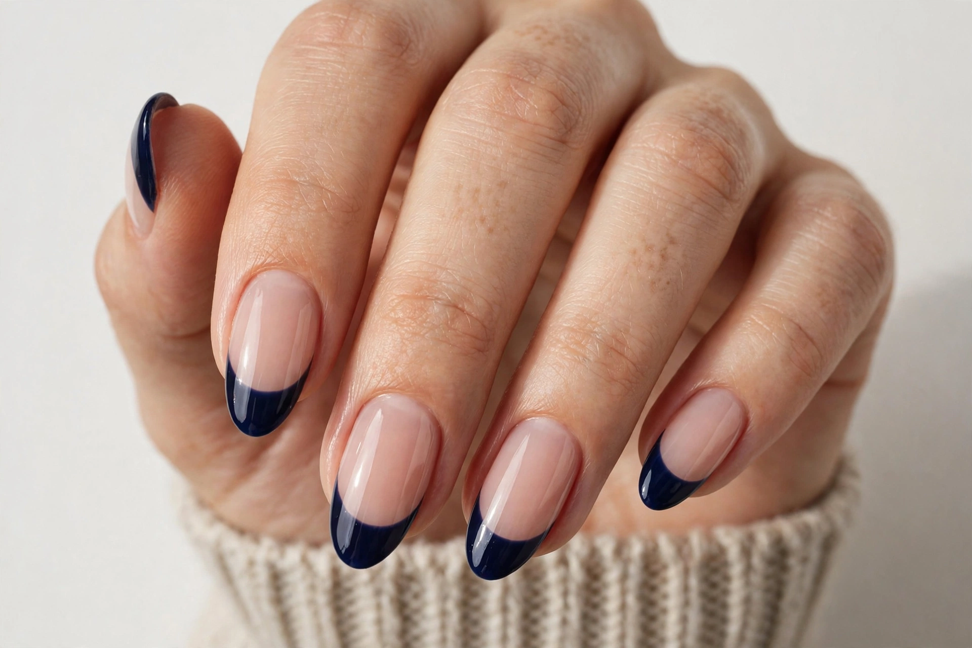 Winter French tip nails with deep navy blue glossy tips on a sheer nude base, shown on medium almond nails.