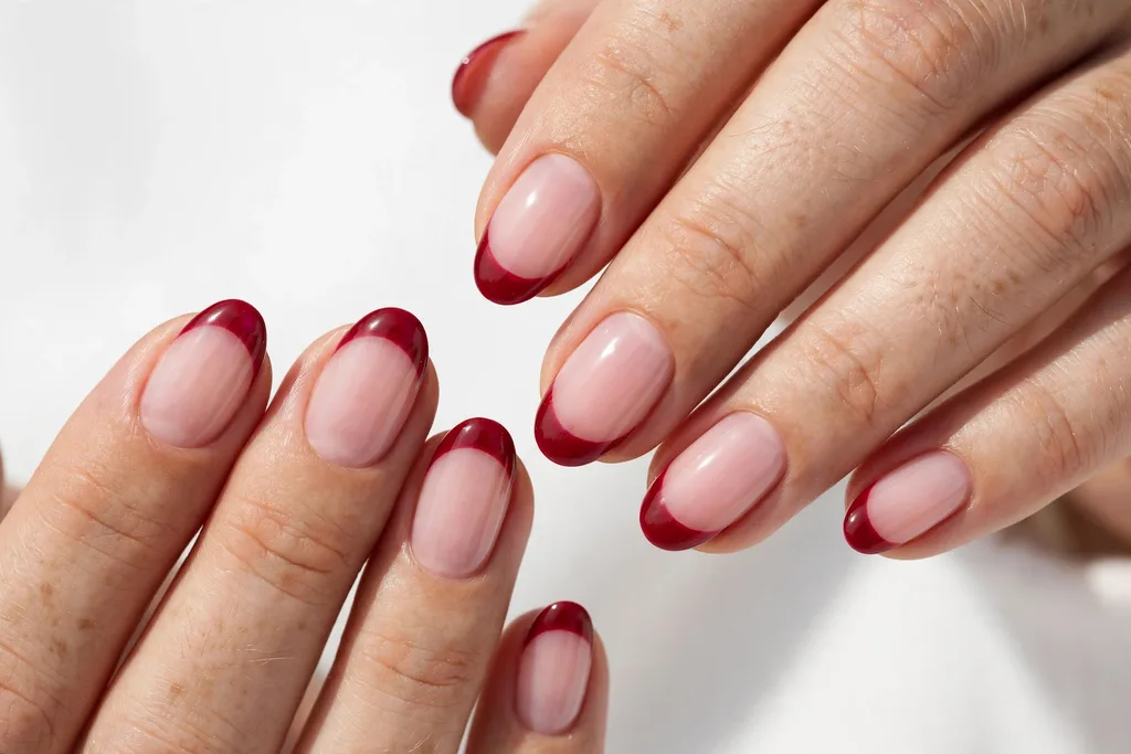 Winter holidays French tip nails with cranberry red glossy tips on a sheer pink base, shown on medium oval nails.