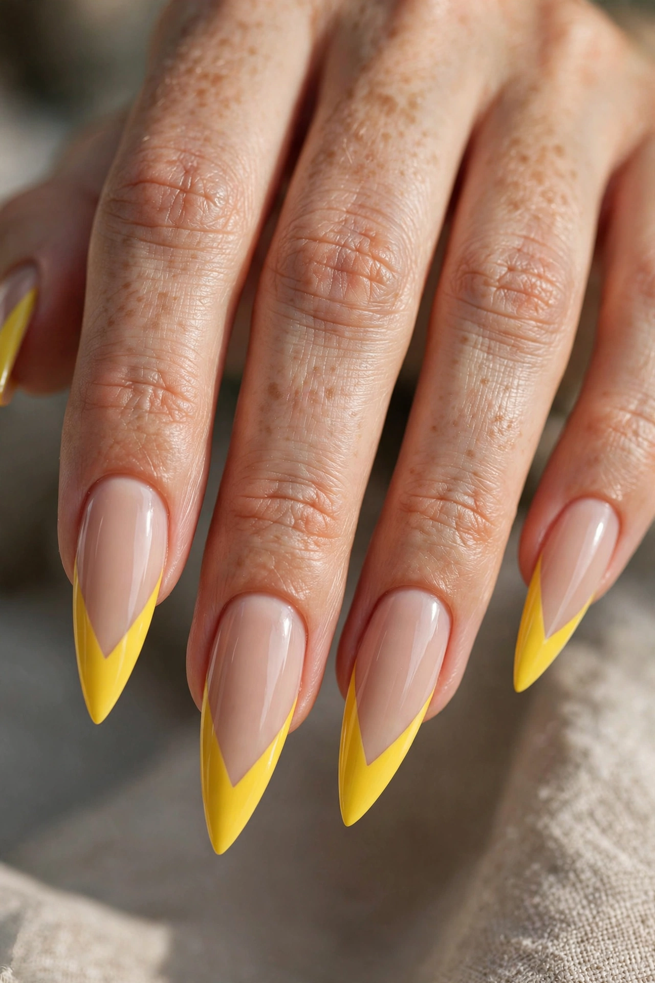 Long stiletto nails with bright yellow V-cut French tips over a nude base.